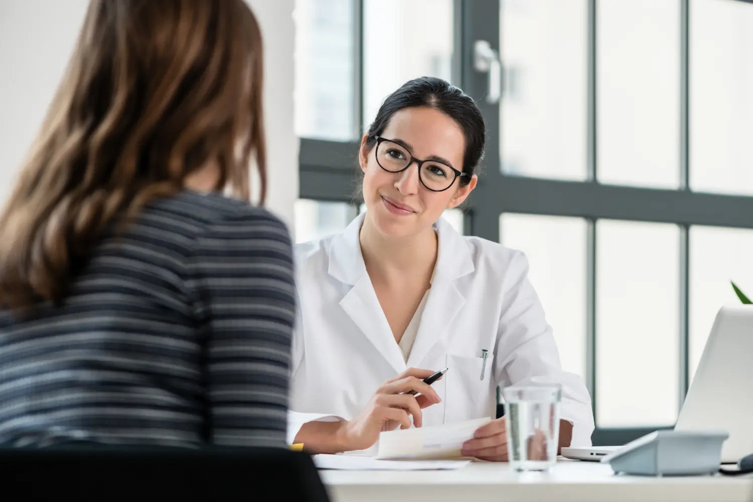 Eine Ärztin hört ihrer Patientin während der Konsultation zu, während sie in einem Büro eines modernen medizinischen Zentrums sitzt